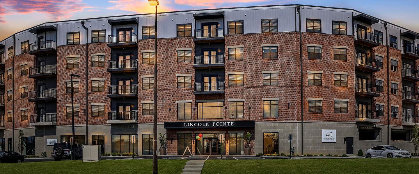 A front-view of an apartment building with inviting landscaping details including trees and bushes.