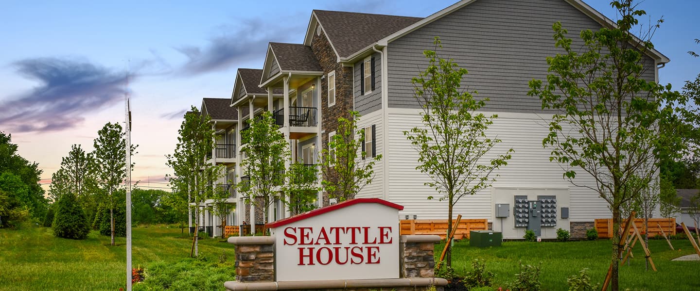 A front-view of an apartment building with inviting landscaping details including trees and bushes.
