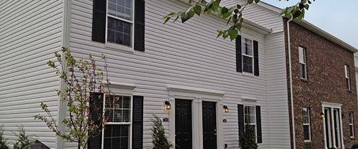 A front-view of an apartment exterior with inviting landscaping details including trees and bushes.