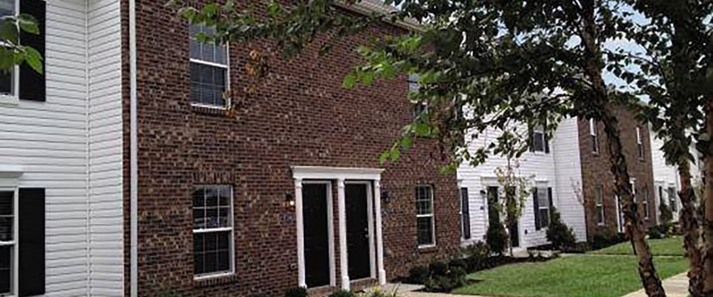 A front-view of an apartment exterior with inviting landscaping details including trees and bushes.