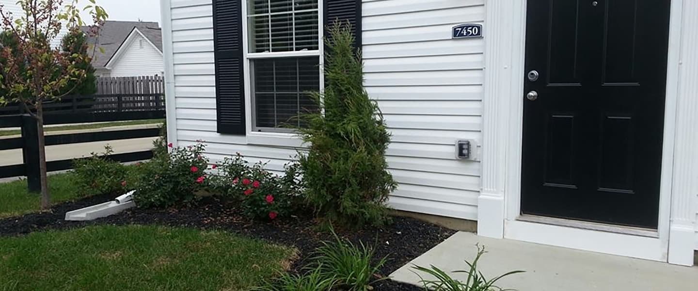 A front-view of an apartment exterior with inviting landscaping details including trees and bushes.
