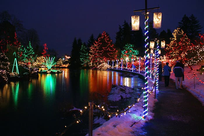 Colorful Christmas light display reflecting on a pond at night near Columbus apartments, with snow-dusted paths and illuminated trees.