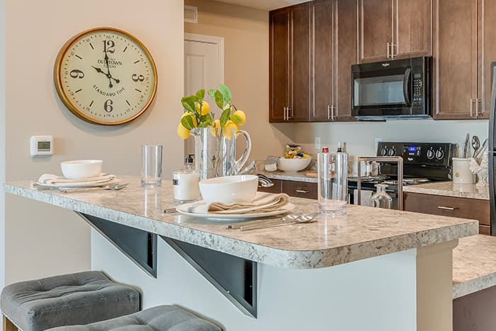Modern apartment kitchen with granite island, dark wood cabinets, Whirlpool appliances, and decorative lemon centerpiece at Cornerstone Village apartments.