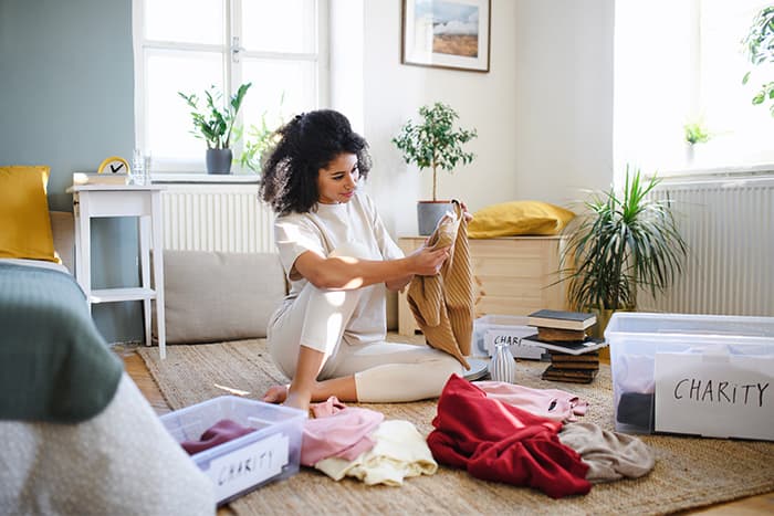 Woman sorting clothes into charity donation bins while decluttering her apartment living room floor.