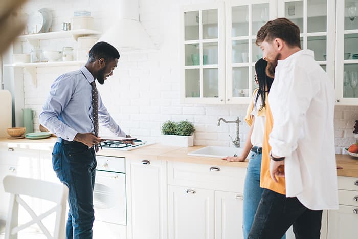Real estate agent showing a modern white kitchen to a couple during their first apartment tour