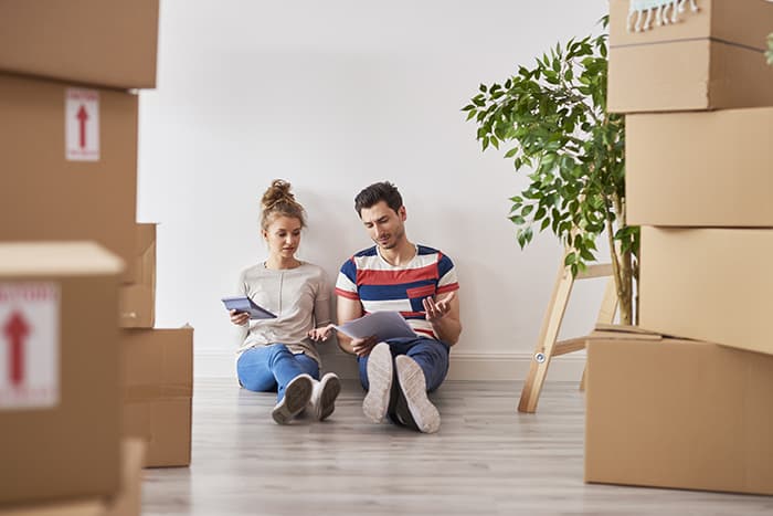 Couple sitting on floor surrounded by moving boxes reviewing moving expenses and paperwork in new apartment