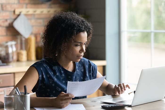 Young woman reviewing renters insurance documents on laptop at home in her apartment
