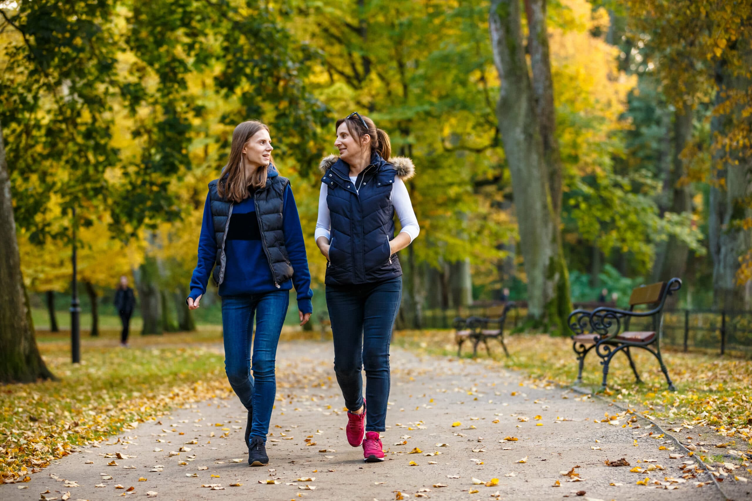 Two women walking on a park path while talking to one another.