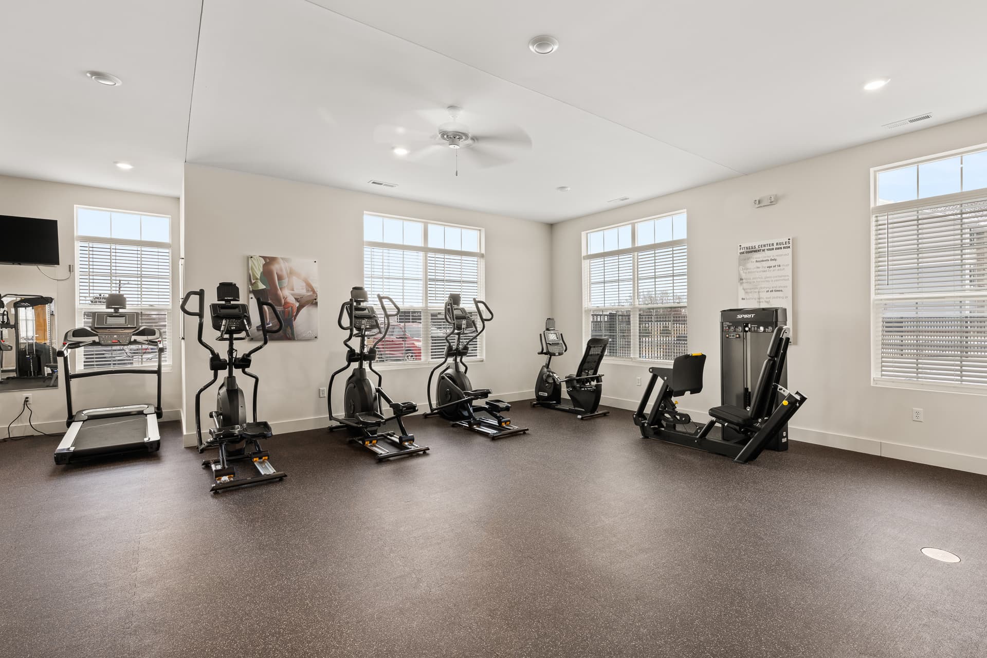 Spacious apartment fitness center with ellipticals, stationary bikes, and leg press machine