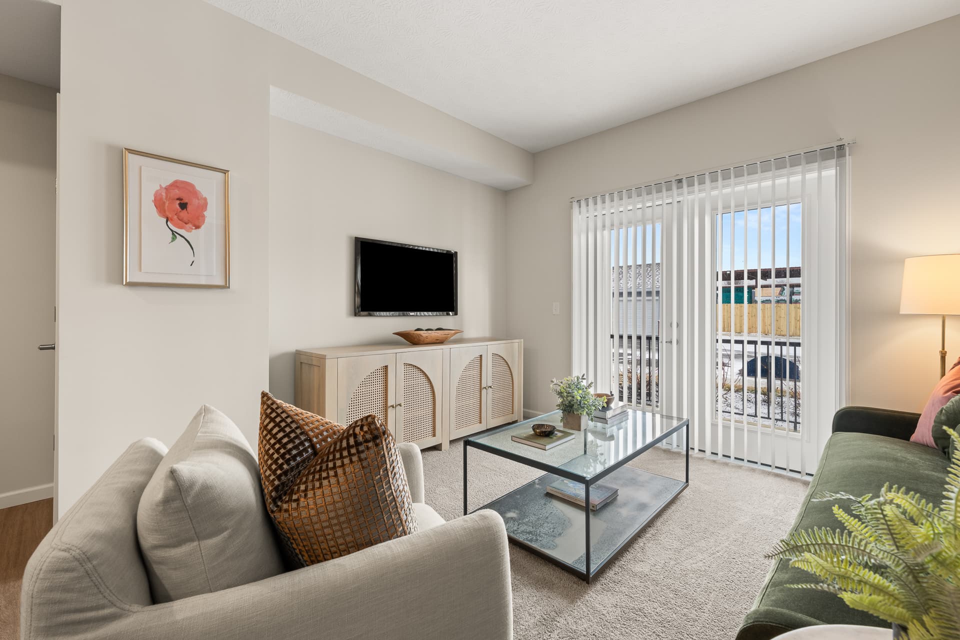 Cozy apartment living room with glass coffee table, wall-mounted TV, and sliding glass balcony door
