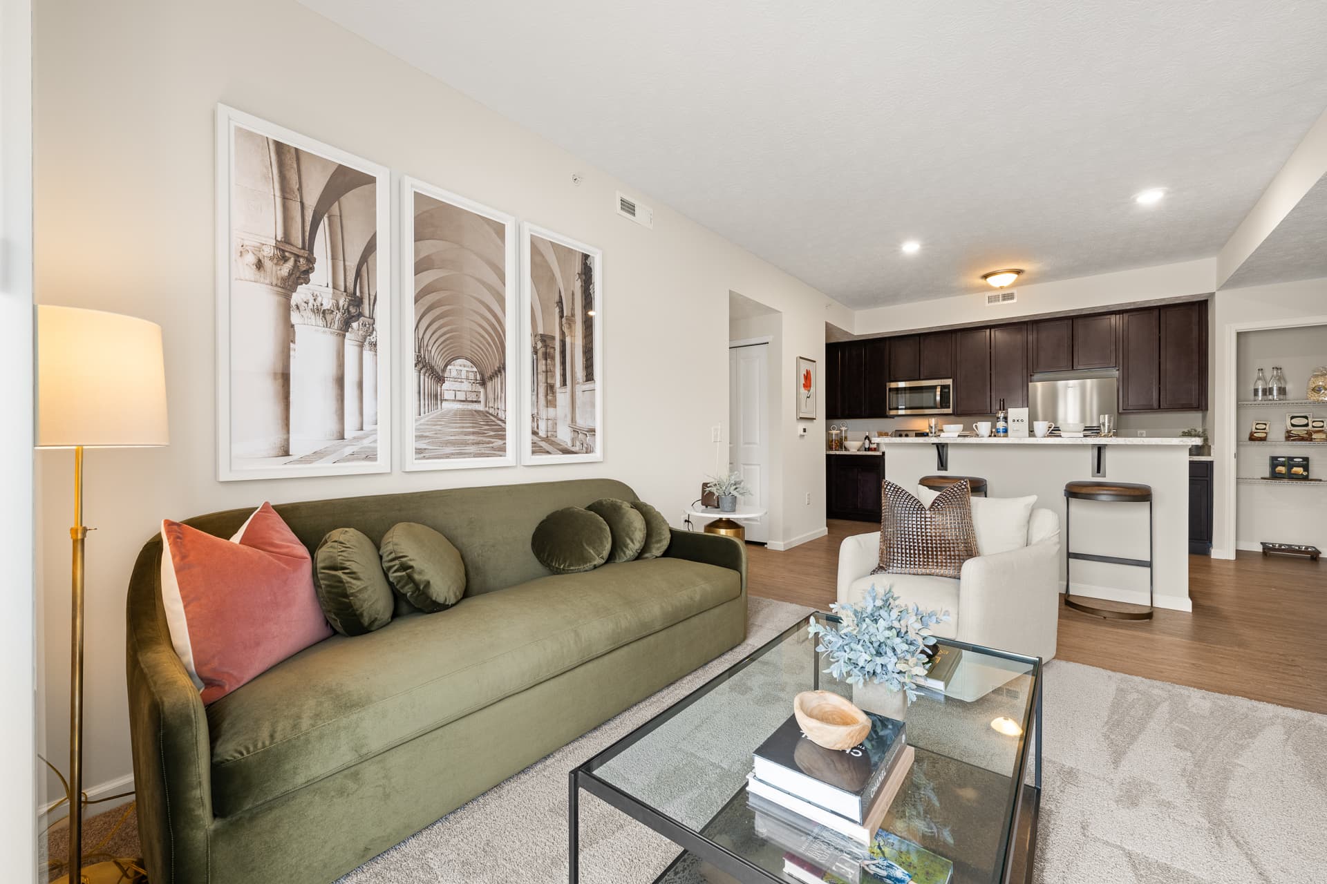 Open-concept apartment living room with green sofa and dark-cabinet kitchen with breakfast bar