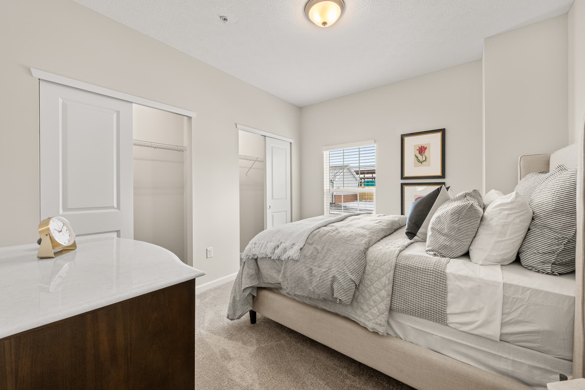 Bright apartment bedroom with plush bedding, dual sliding closets, and a marble-top dresser
