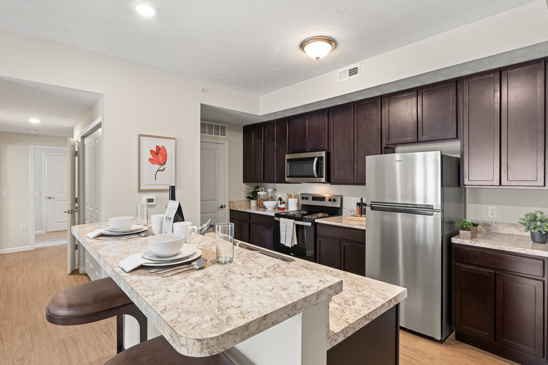Spacious apartment kitchen featuring dark cabinetry, stainless appliances, and granite island with bar stools