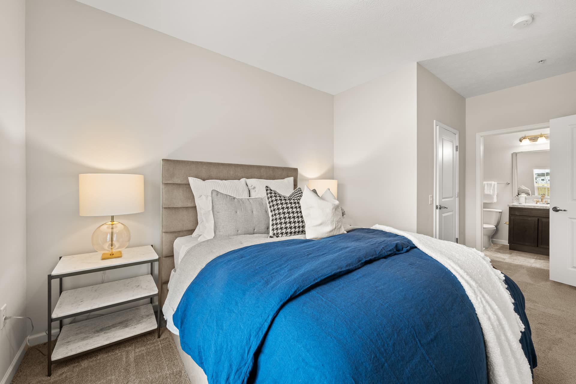 Cozy apartment bedroom with blue bedding, upholstered headboard, and en-suite bathroom view