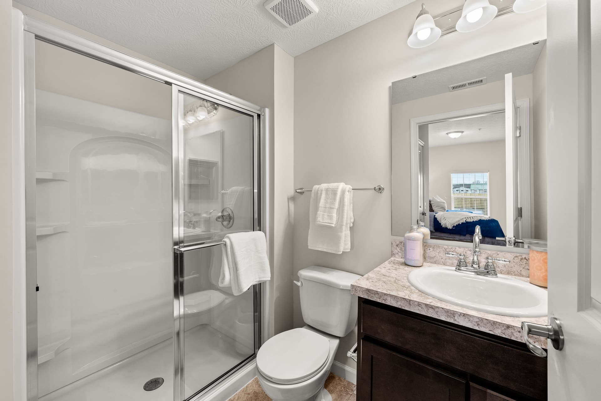 Apartment en-suite bathroom featuring walk-in glass shower, dark vanity, and large mirror