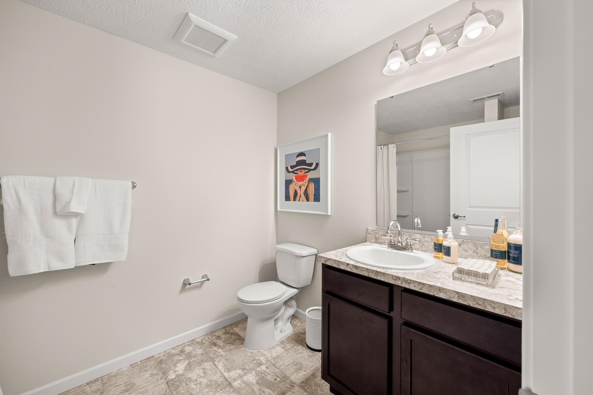 Apartment full bathroom with dark vanity, granite countertop, toilet, and decorative wall art