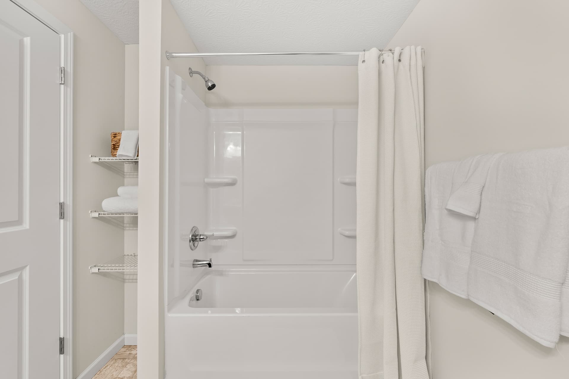 Bright apartment bathroom with white tub-shower combo, curtain, and built-in shelving