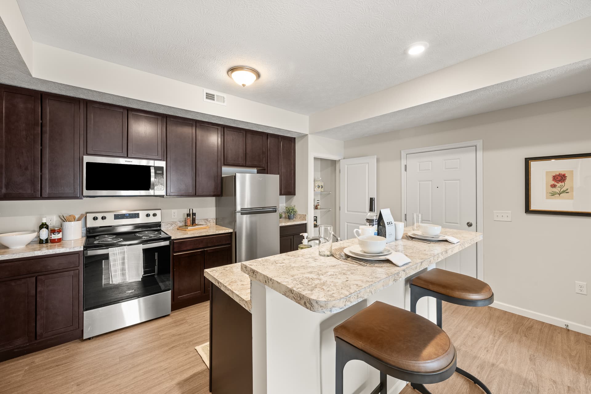 Apartment kitchen with dark cabinets, stainless steel appliances, and granite breakfast bar seating