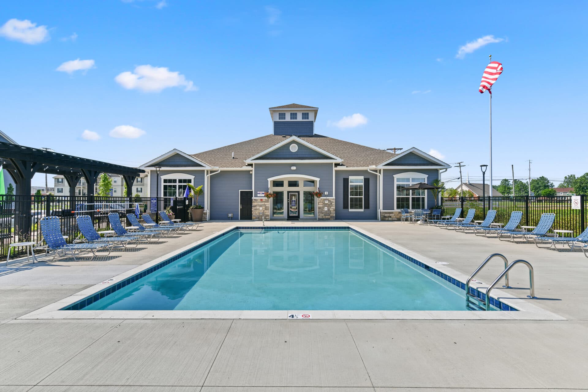 Outdoor pool and clubhouse at Ardent apartments with lounge chairs and pergola under blue skies