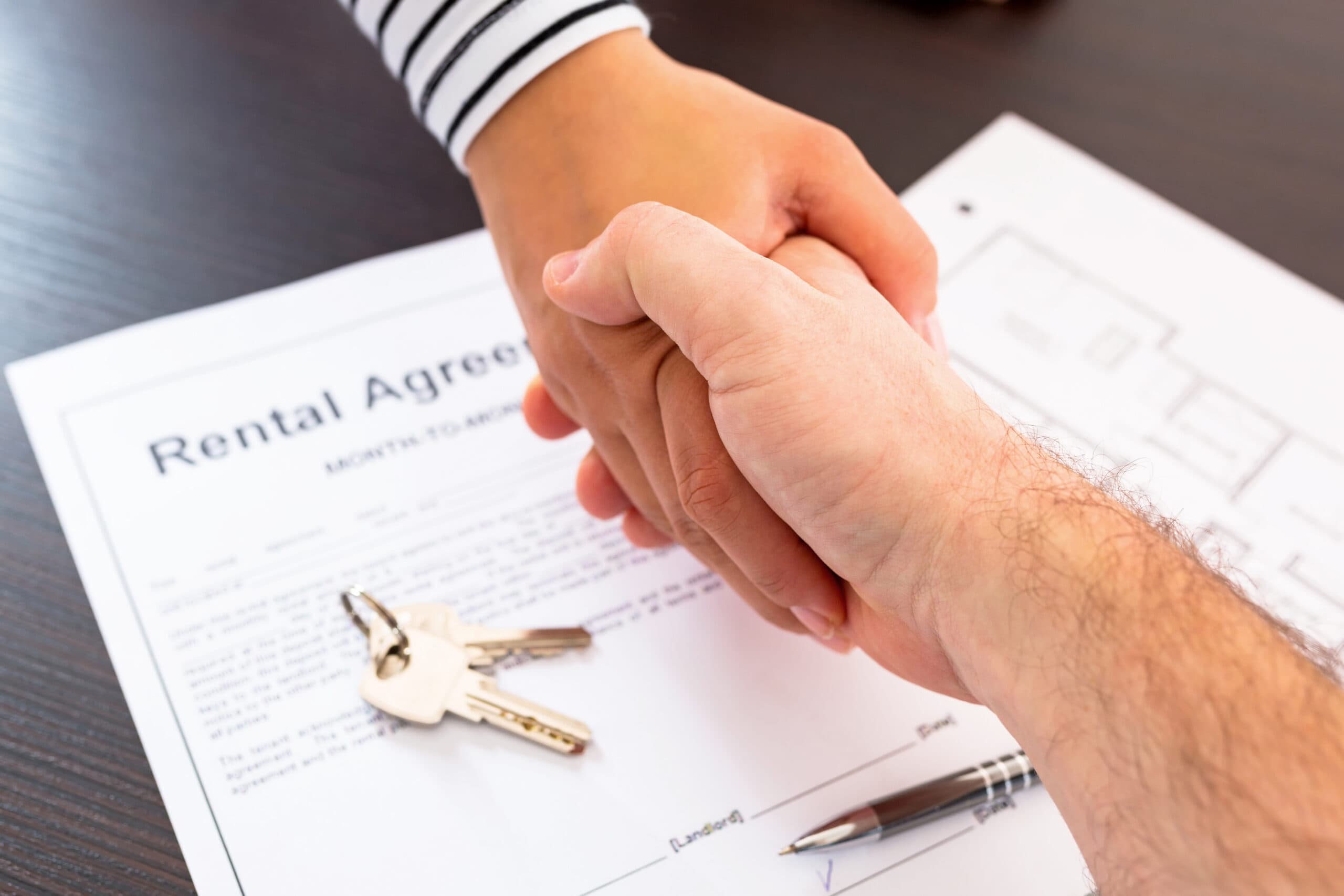 Two people shaking hands and exchanging keys over a rental agreement