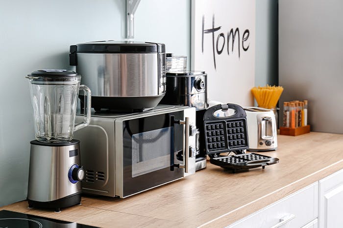 A blender, microwave, rice cooker, and waffle maker on a kitchen counter