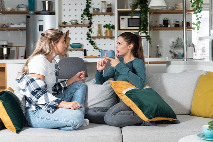 Two female roommates arguing on a sofa in an apartment living room