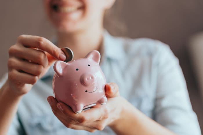 A young woman sliding a coin into a piggy bank.